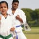 A girl in a karate uniform with a green belt, and a boy with a blue belt behind her, doing a controlled punch movement